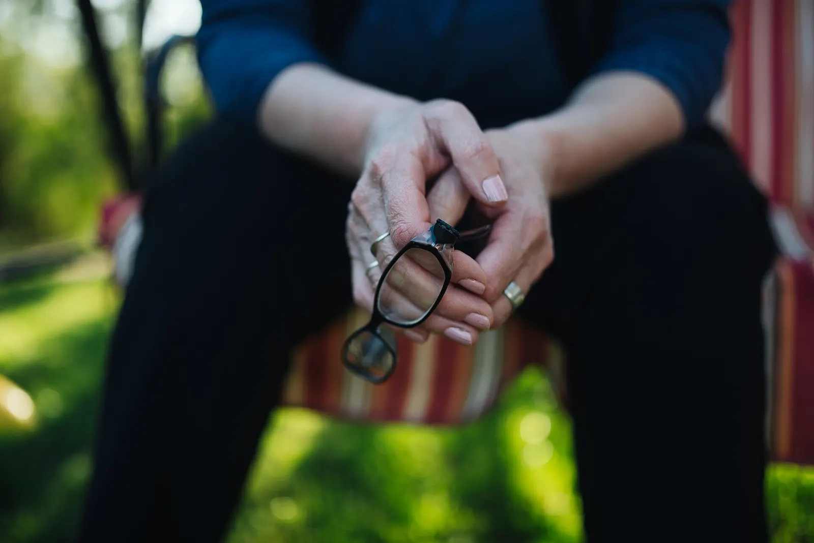 Hands holding a pair of glasses in the lap, outdoors