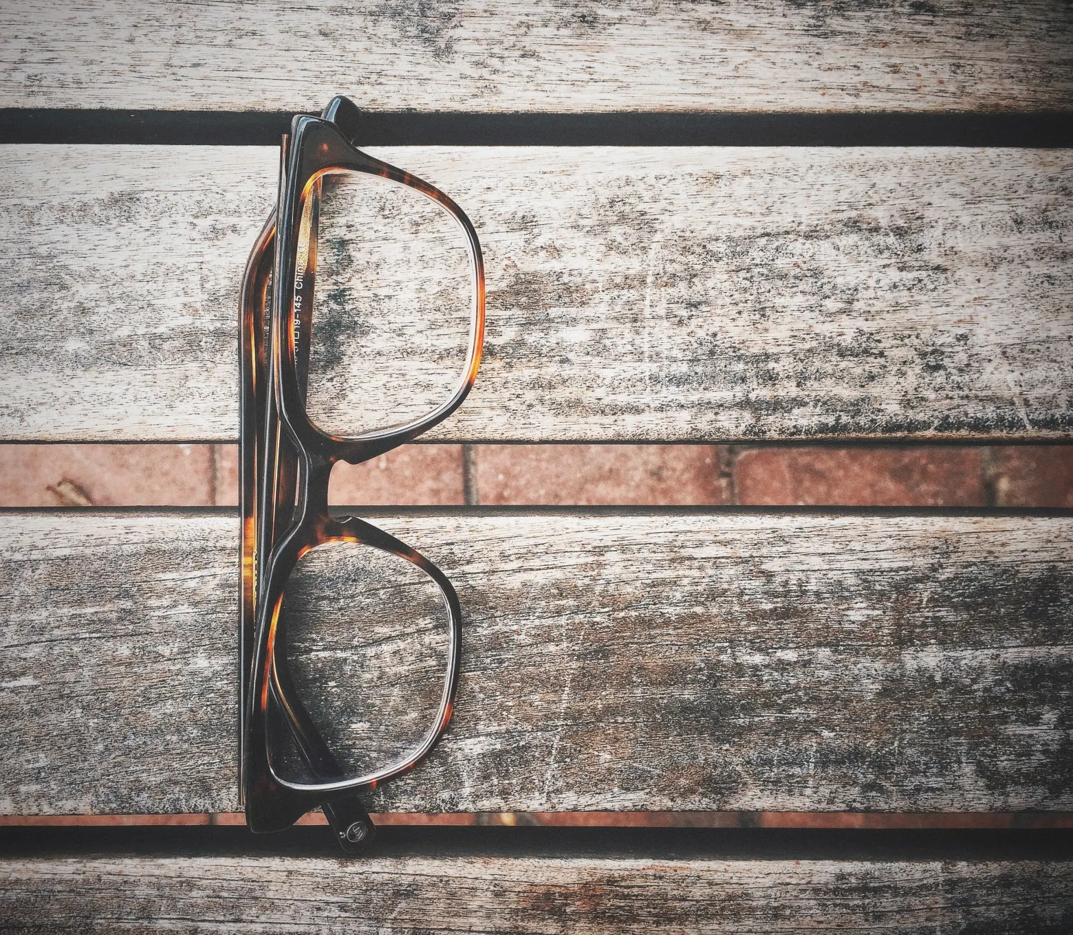 Pair of tortoiseshell glasses resting on a weathered wooden bench