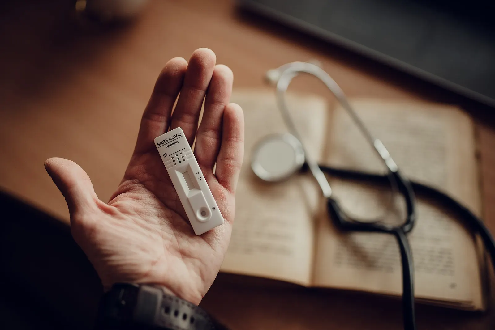 Hand holding a test device beside a stethoscope and an open notebook