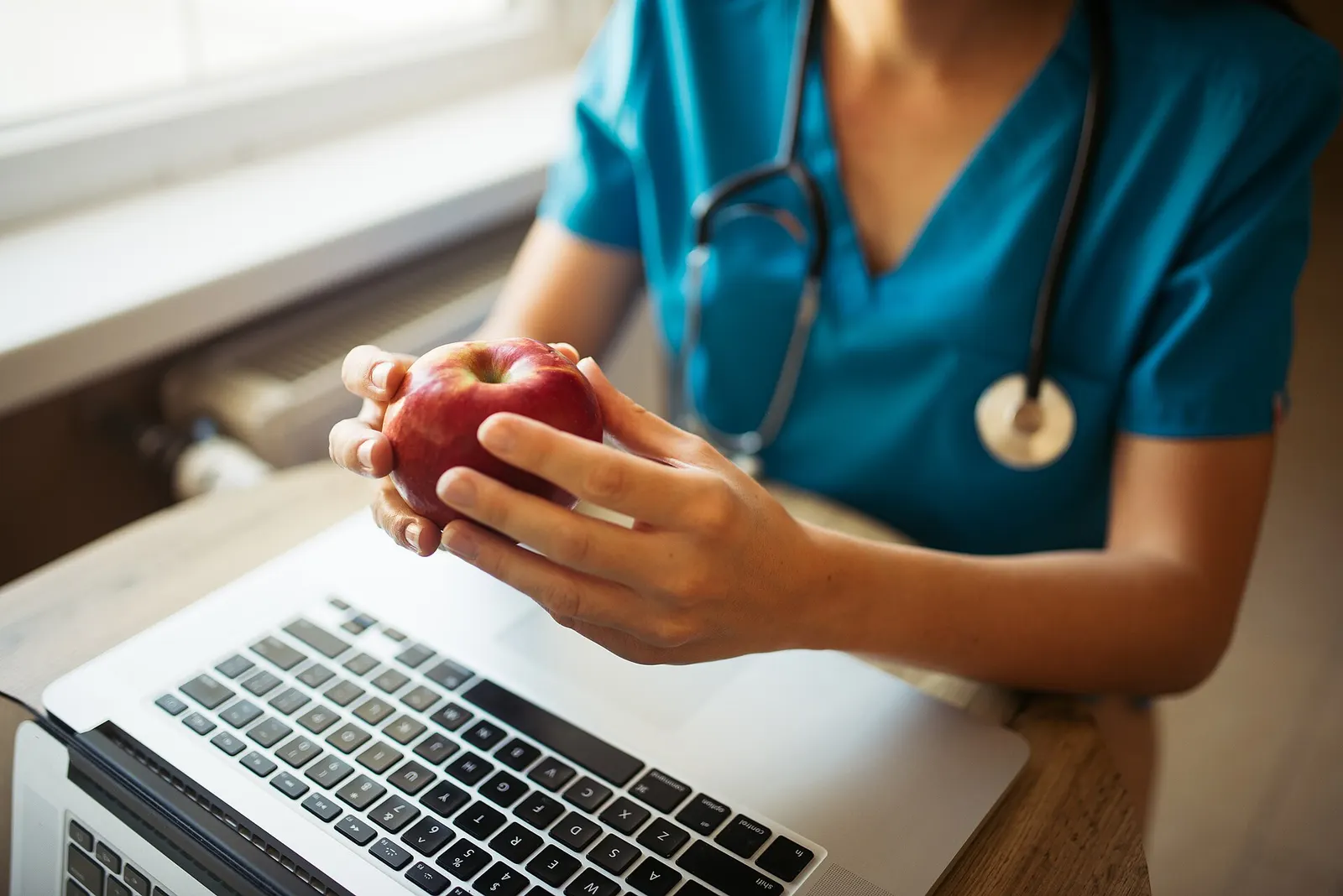 Nurse in scrubs with a stethoscope working at a laptop