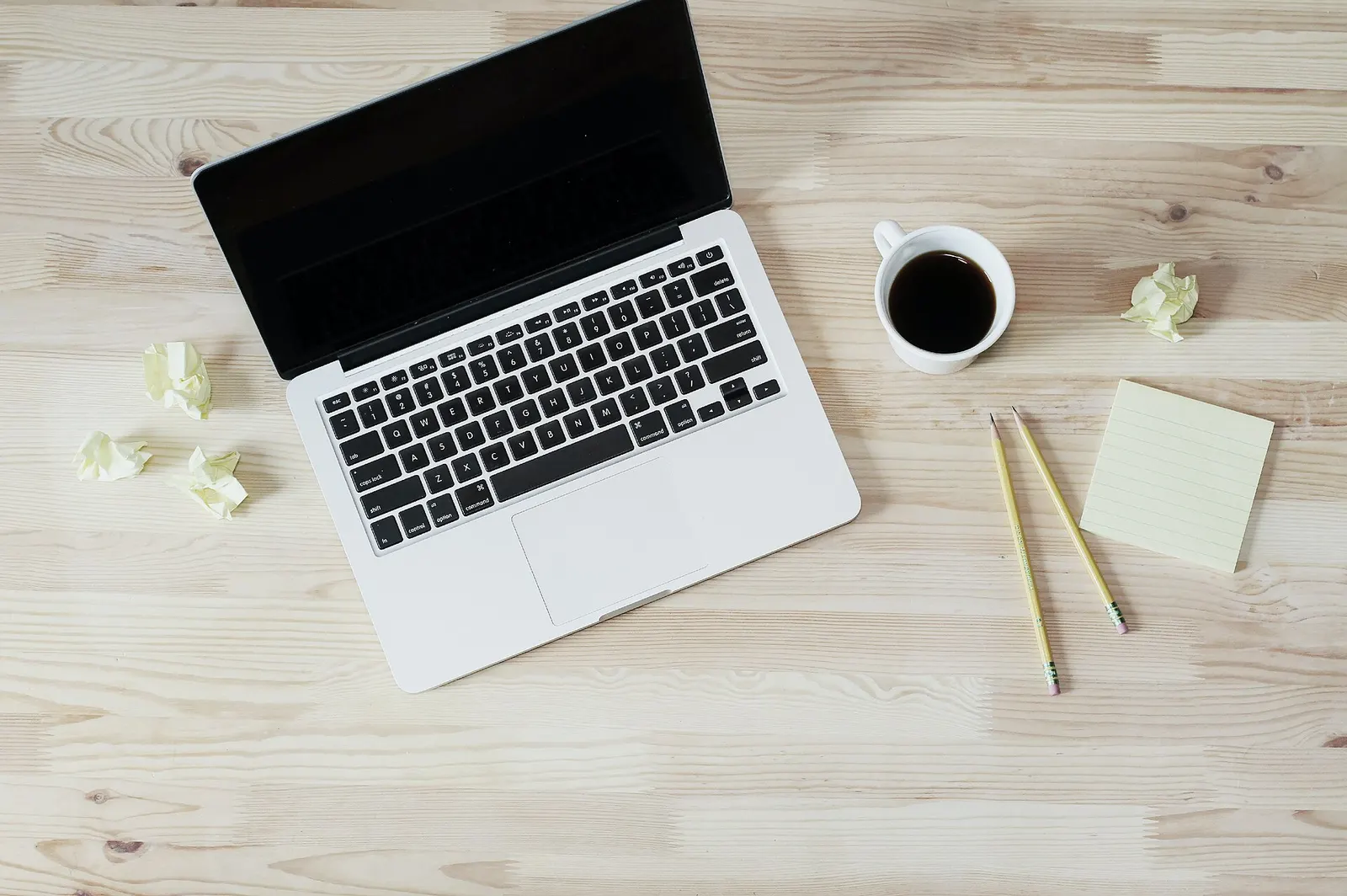Laptop, coffee cup and pencils on a pale wooden desk seen from above
