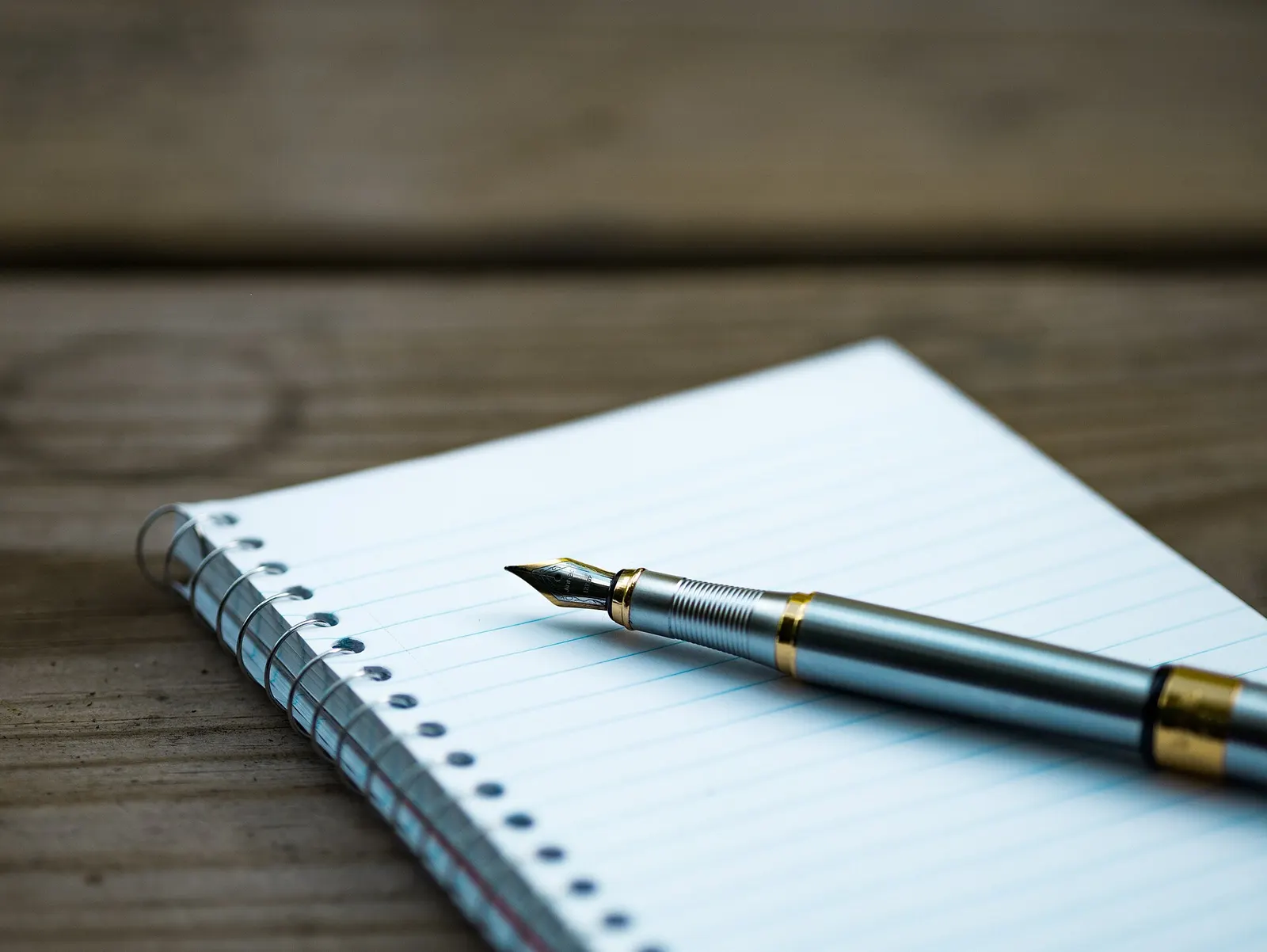 Fountain pen resting on a blank lined notepad on a wooden desk, ready to sign an application